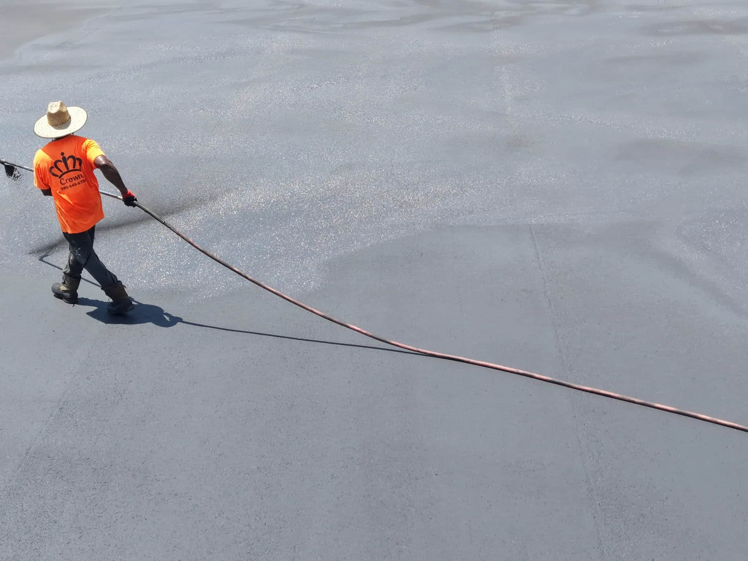 A Crown Paving crew member spraying sealer across a commercial truck yard