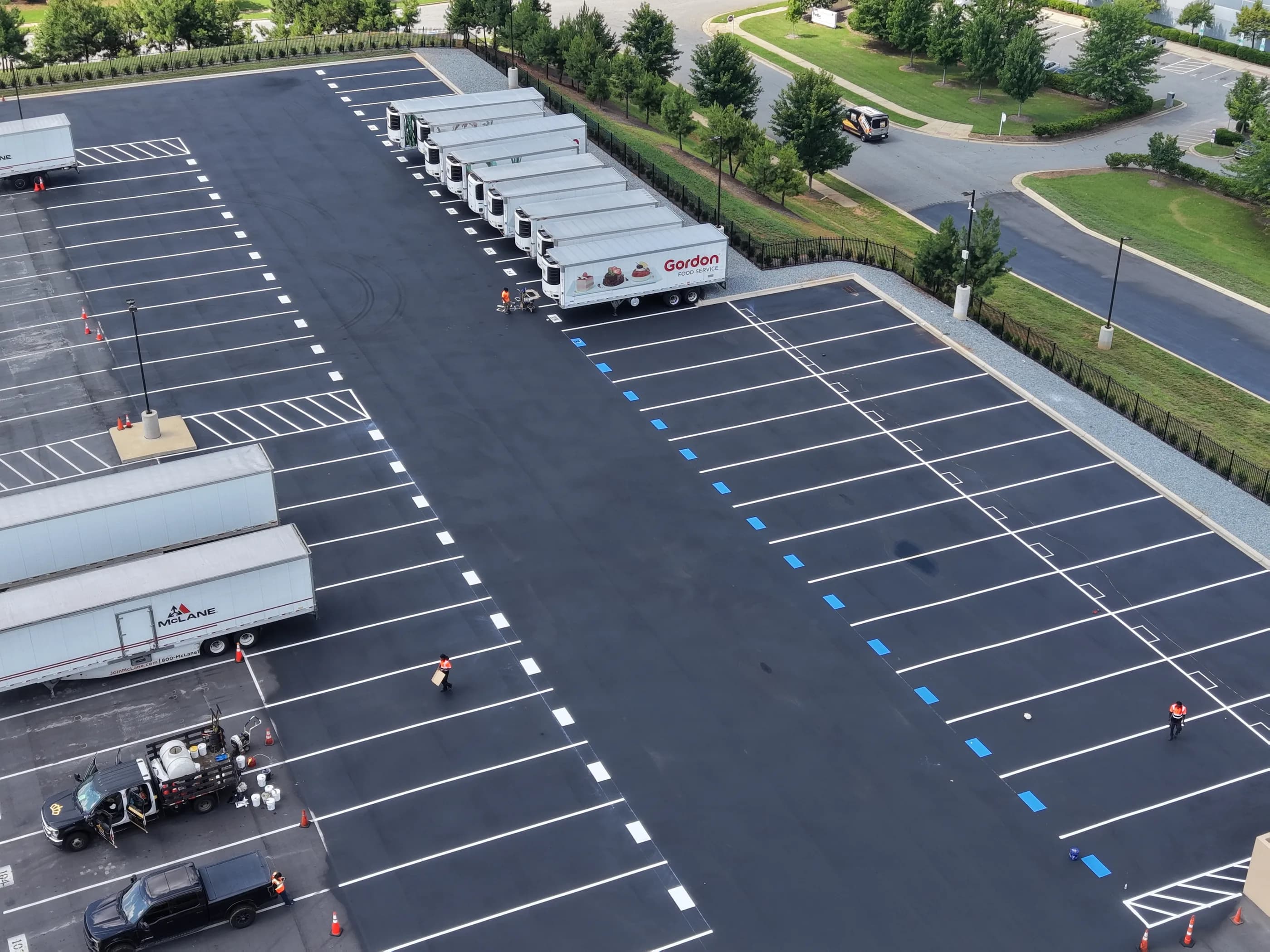 An aerial view of a freshly striped distribution center yard, with white stalls, blue accessible spaces, hatched loading zones and refrigerated trailers backed into the docks