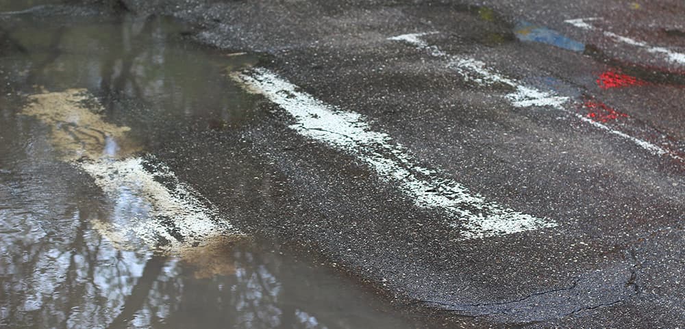 Standing water and cracking across a weathered parking lot