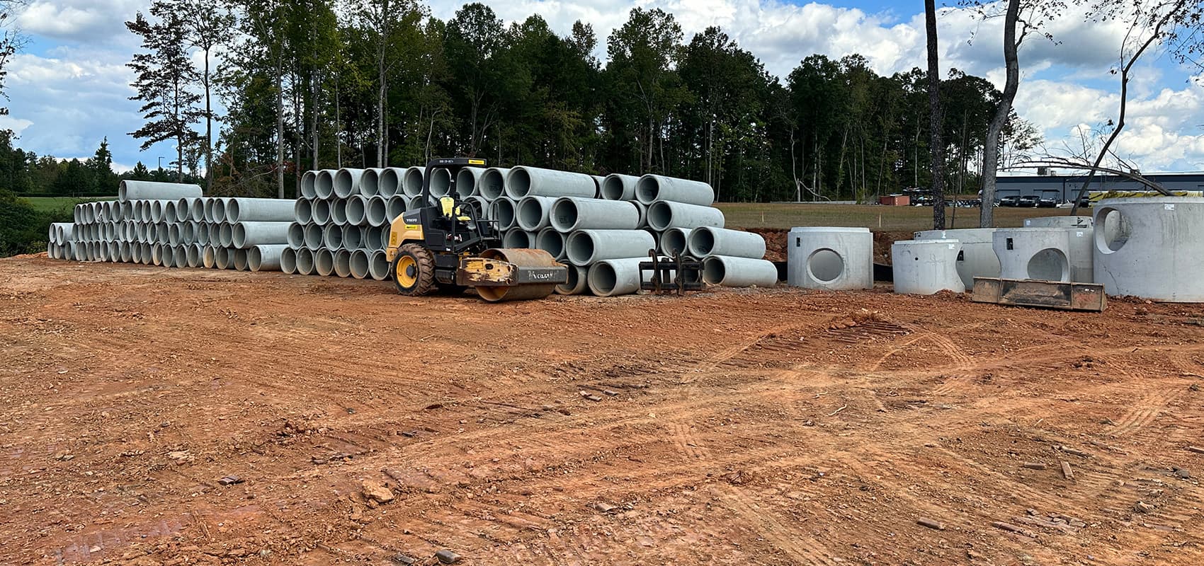 Precast concrete pipe and catch basin structures staged on a graded site