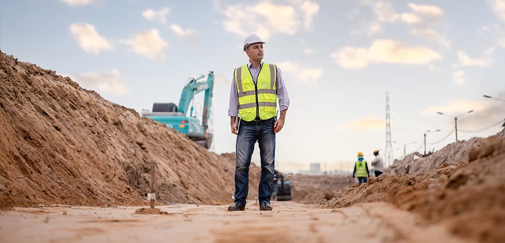 A site engineer in a hard hat and high-visibility vest standing at an excavation