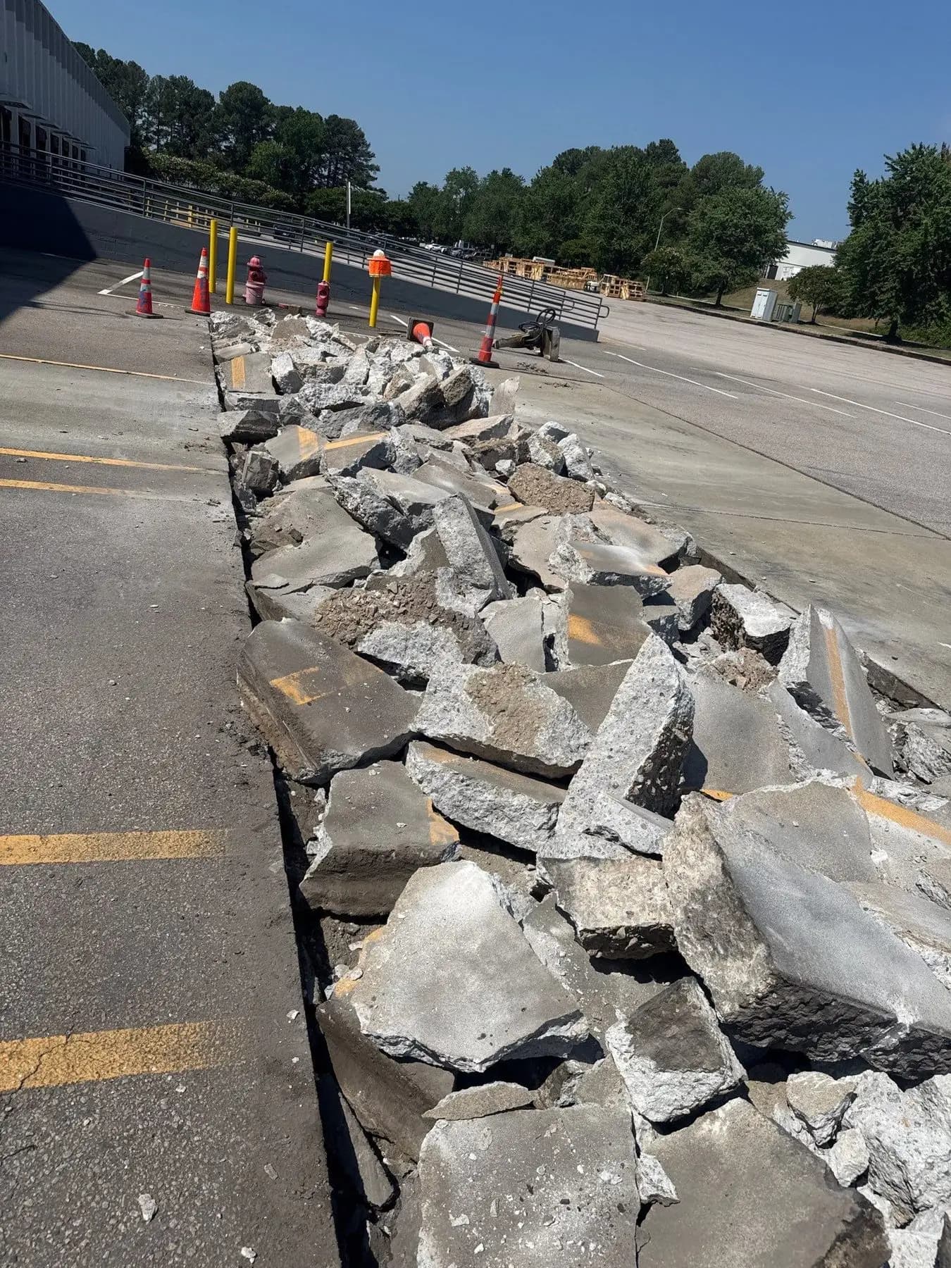 Broken-out concrete curb and pavement windrowed in a warehouse truck court in Raleigh, NC