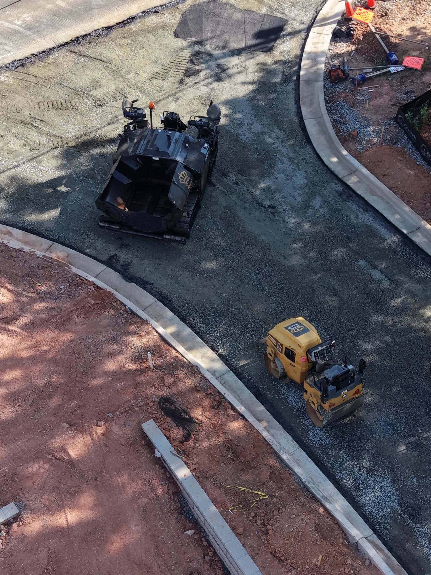 Paver and roller laying and compacting a fresh asphalt mat, seen from above