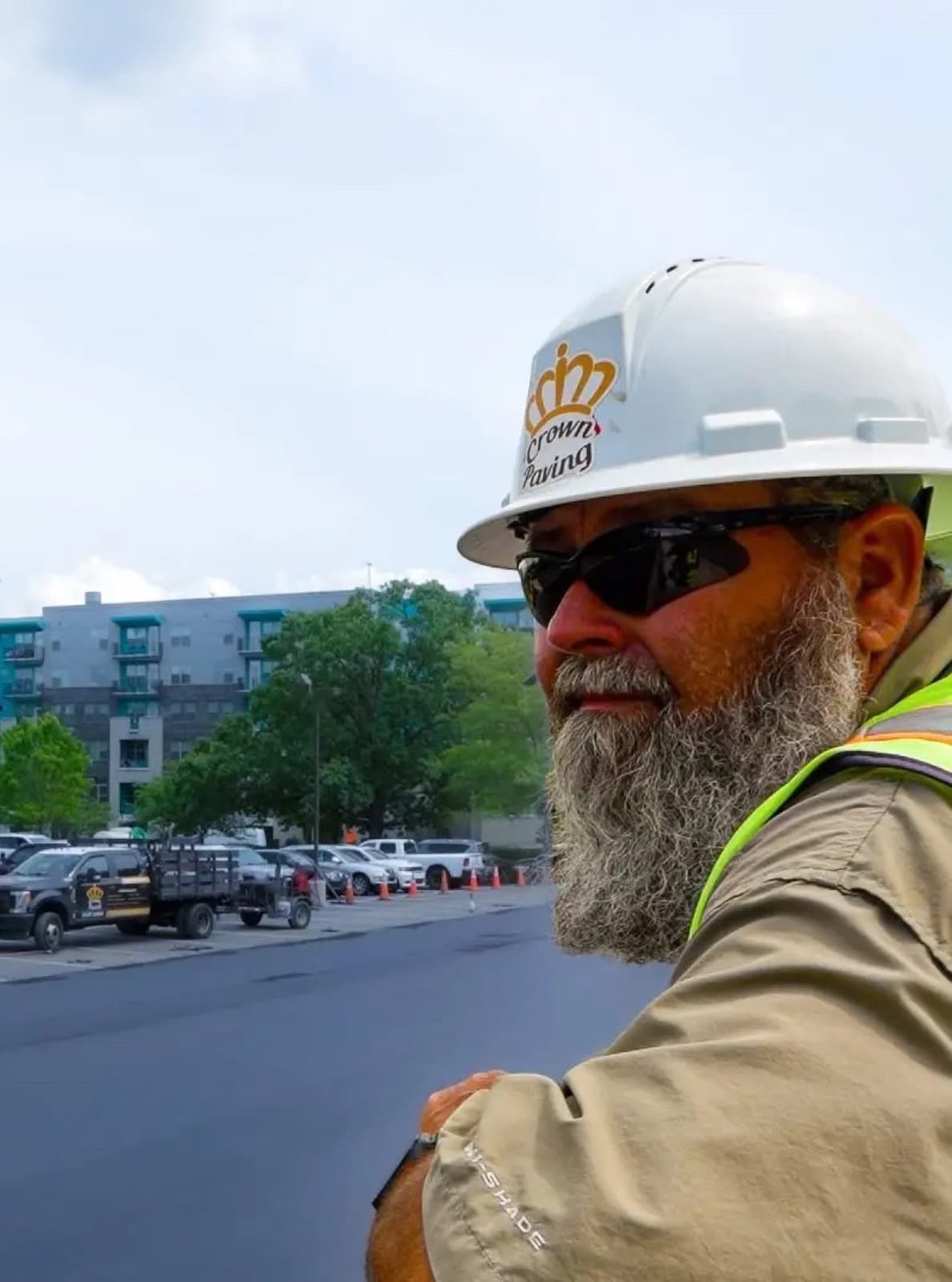 A Crown Paving crew member in a branded hard hat on a live job site, with the company's milling machine and truck behind him