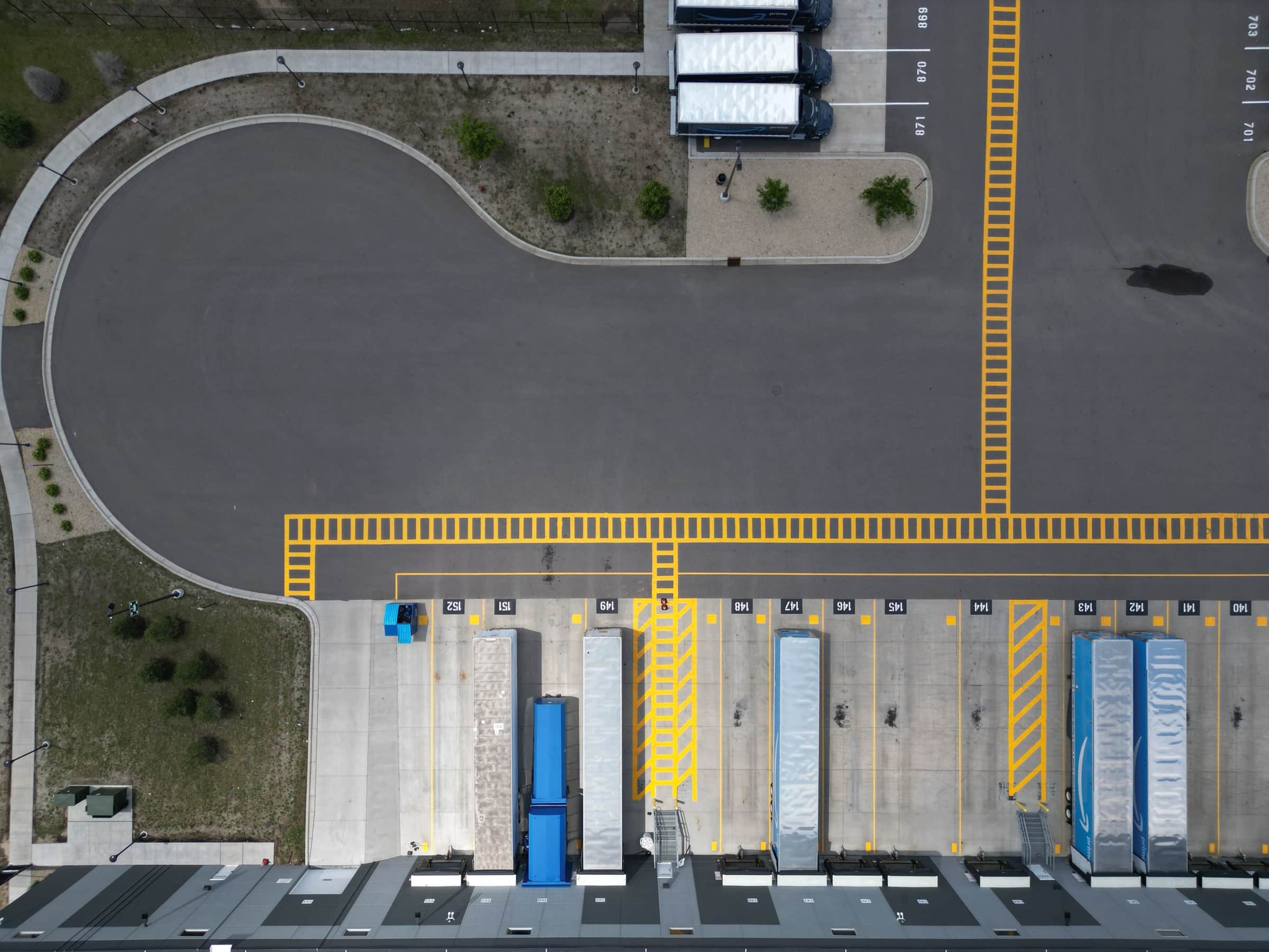 A distribution center truck court from above, with numbered dock bays and hatched pedestrian walkways on fresh asphalt