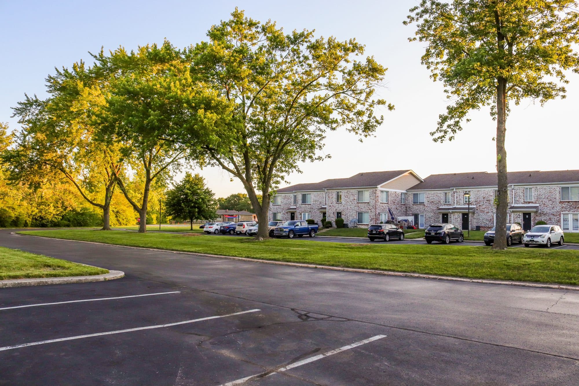 A marked asphalt parking lot in front of a row of brick townhomes in evening light